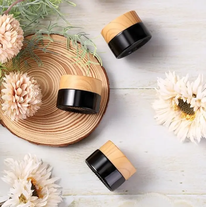 Luxury GHK cream jars with brown bases and natural wood lids styled with soft flowers on a light wood surface.